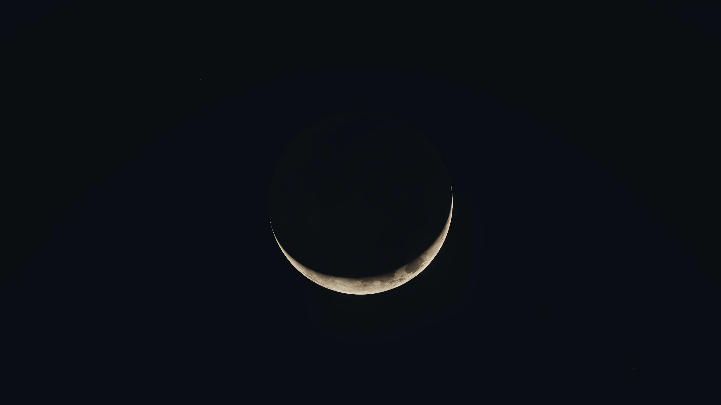 A thin crescent Moon in a dark sky, the rest of its disc just visible in earthshine